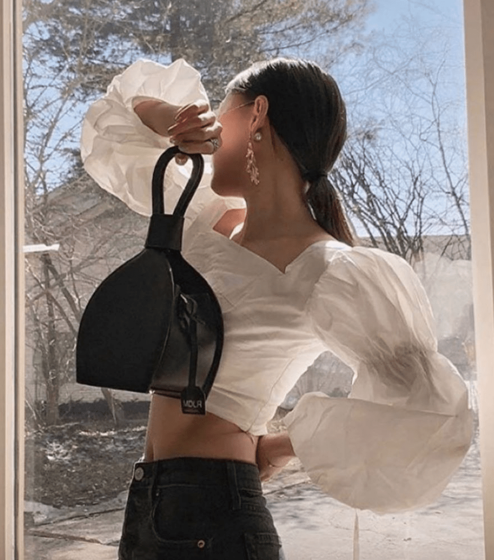 a woman in white clothes holding ATENA BLACK PURSE-SLING BAG, a black bag, handbag with minimalist look from Marie De La Roche